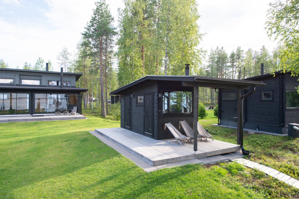 Salvos Combi black outdoor sauna on the lawn, with a deck and two lounge chairs