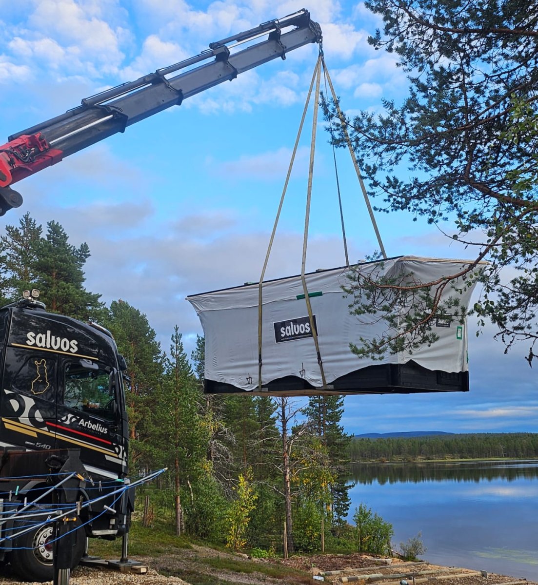 Suojapeitteeseen kääritty Salvos-rakennus nostetaan nosturilla rannan rakennuspaikalle