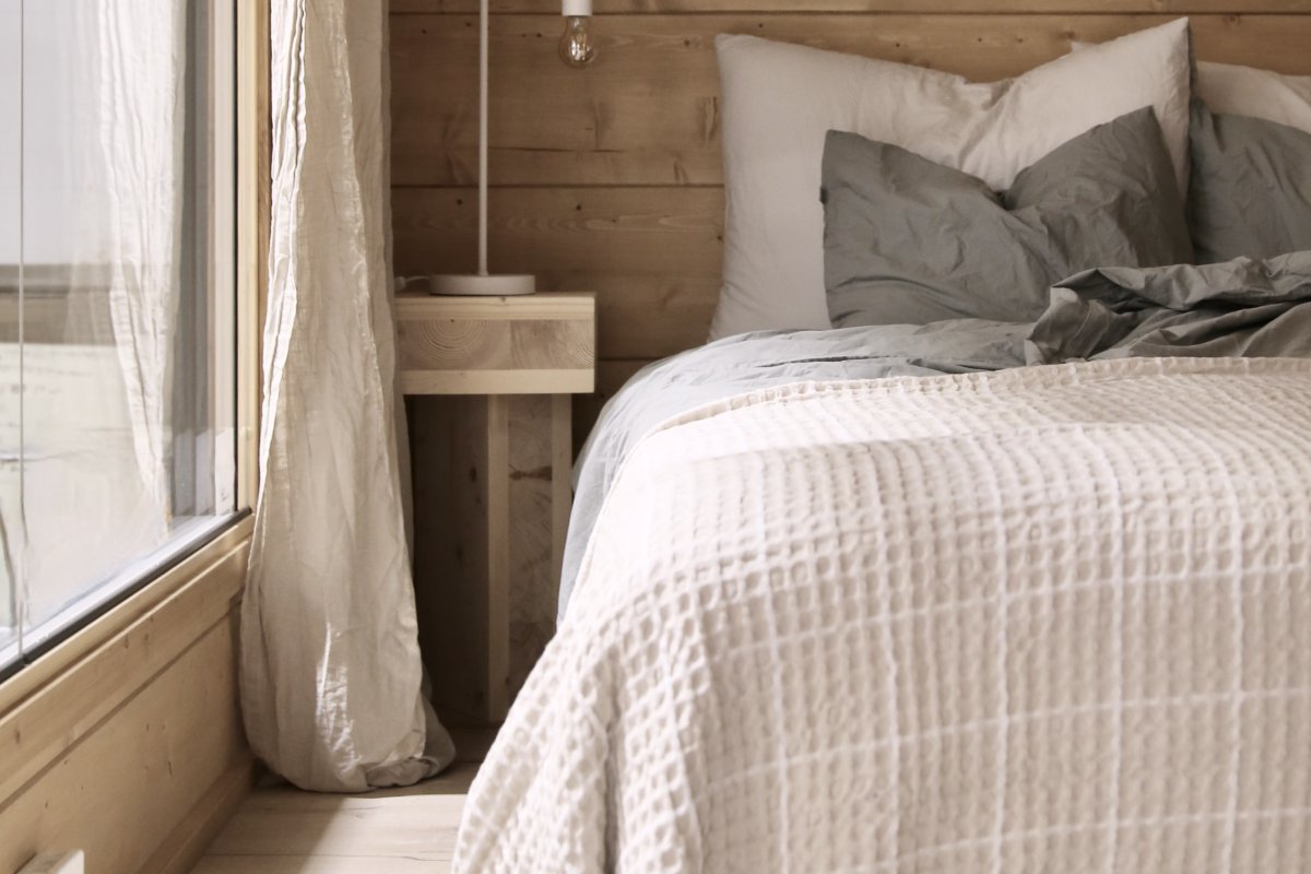 Bedroom with log walls in a Salvos sauna cabin, with a bed in light-colored linens next to the window