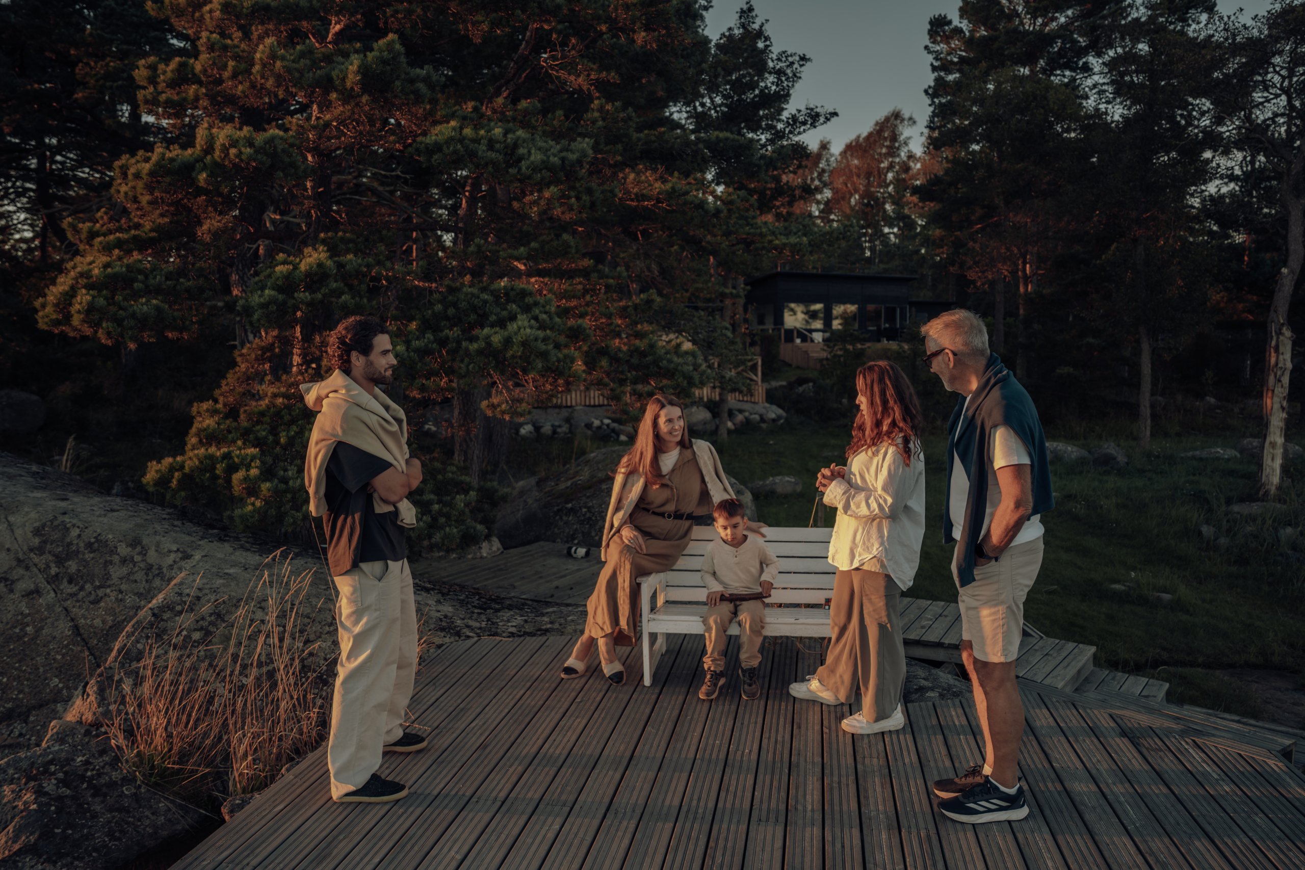 Perhe kokoontunut puuterassille Salvoksen mökin pihassa kalliosaaressa illan kultaisessa valossa