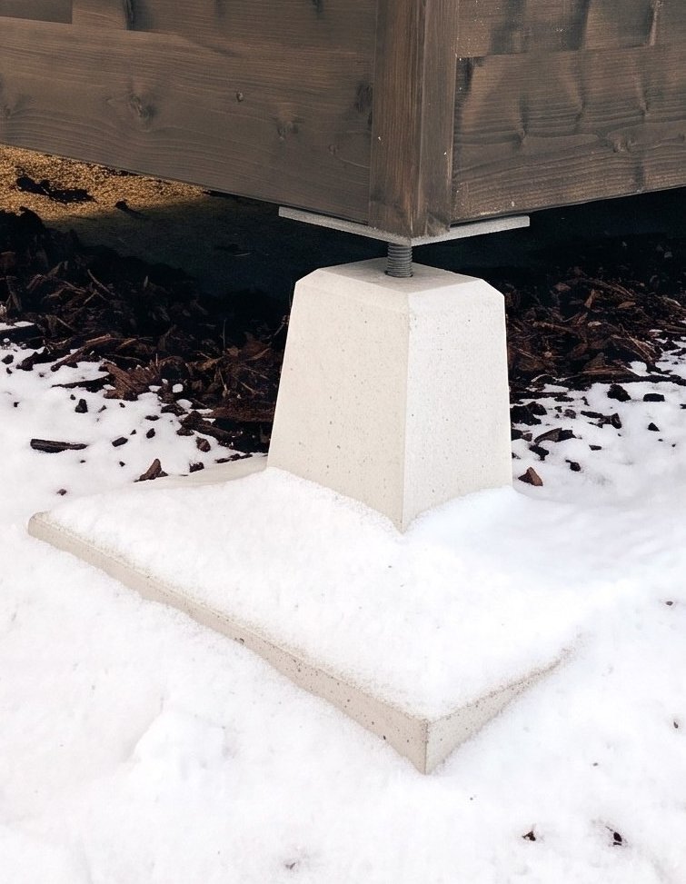 A BCE foundation pillar with an adjustable base under a log building in winter